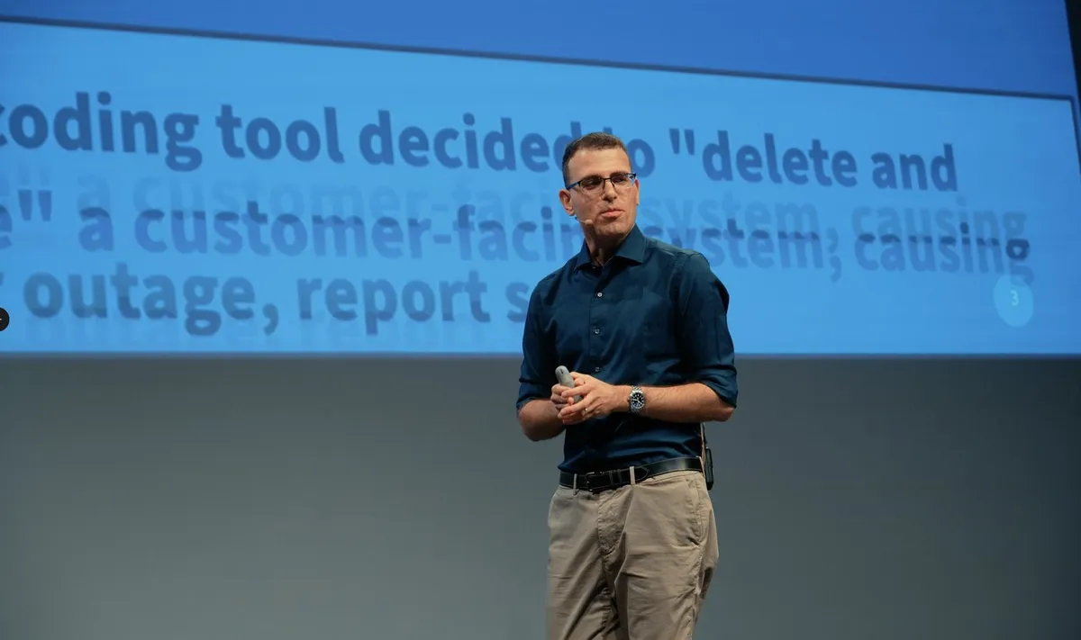 Ran Isenberg on stage presenting a slide about an AI coding tool that deleted a customer-facing system